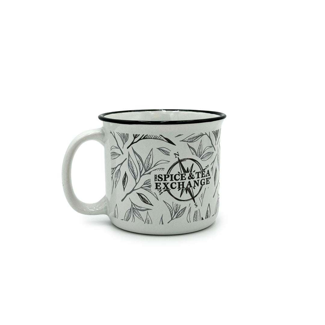 The Tea Leaf Ceramic Camp Mug is a 12-ounce white ceramic mug with a black tea leaf motif, sleek black rim, and The Spice & Tea Exchange logo in bold black lettering on the front. Background is plain white.