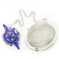 The Infuser with Teapot Charm is a metal tea infuser with a mesh ball and chain, featuring a blue teapot-shaped charm decorated with yellow stars and crescent moons—perfect for loose leaf tea and ideal for tea lovers on the go.