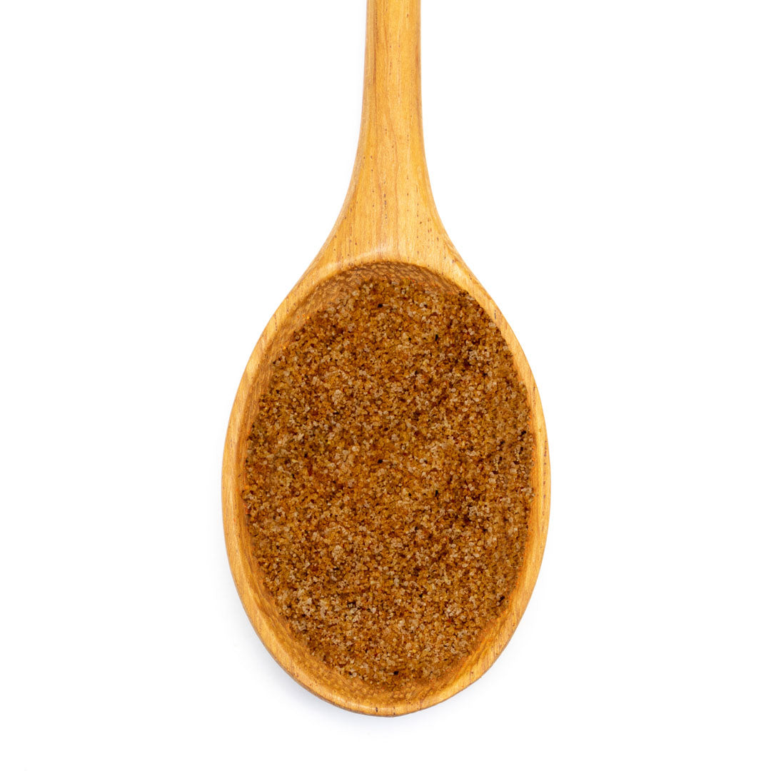 A wooden spoon holds French Fry Seasoning - The Original, a light brown blend ideal for sweet and savory fries, photographed from above on a white background.