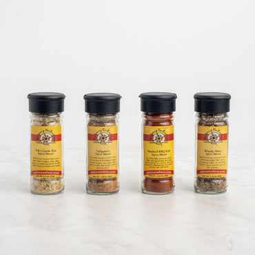 The Totally Tailgating 4-Pack Gift Set features four spice jars with black lids, each with a yellow-and-red label: Garlic Fix, Tailgate, Smoked BBQ Rub, and Bloody Mary—perfect blends for your next tailgate party.