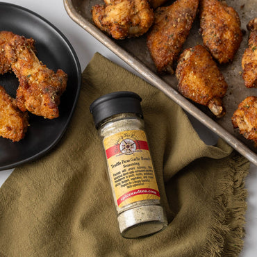 Truffle Parm Garlic Seasoning in flip-top shaker jar next to plate and pan of baked chicken wings and drumsticks