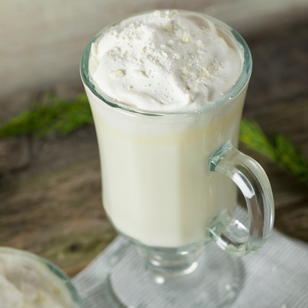 Glass mug filled with a creamy beverage and whipped cream on a wooden surface.