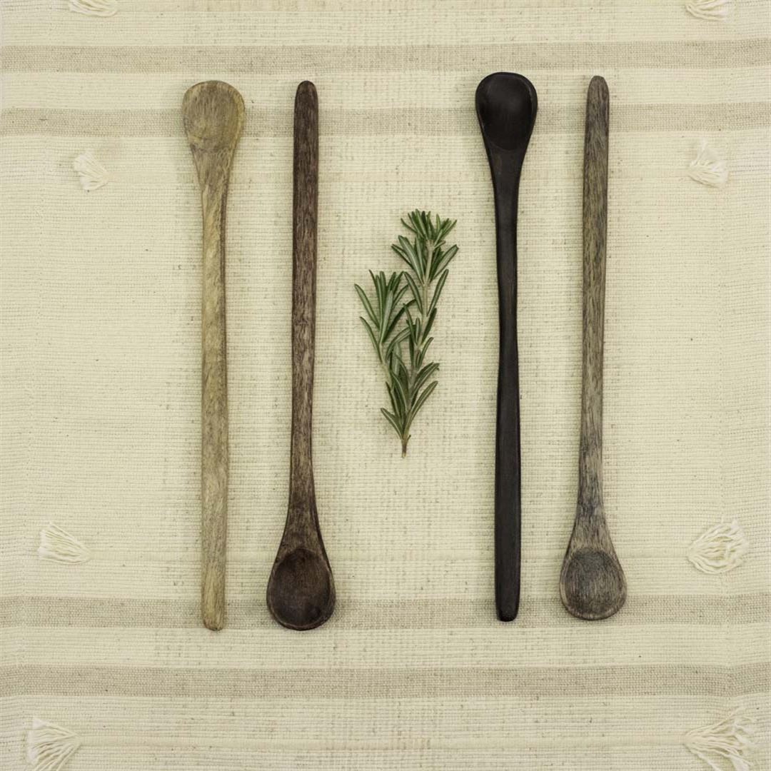 Four Wooden Tasting Spoons, a must-have kitchen essential, are arranged vertically on a beige woven cloth—two per side—with a sprig of rosemary placed in the center.