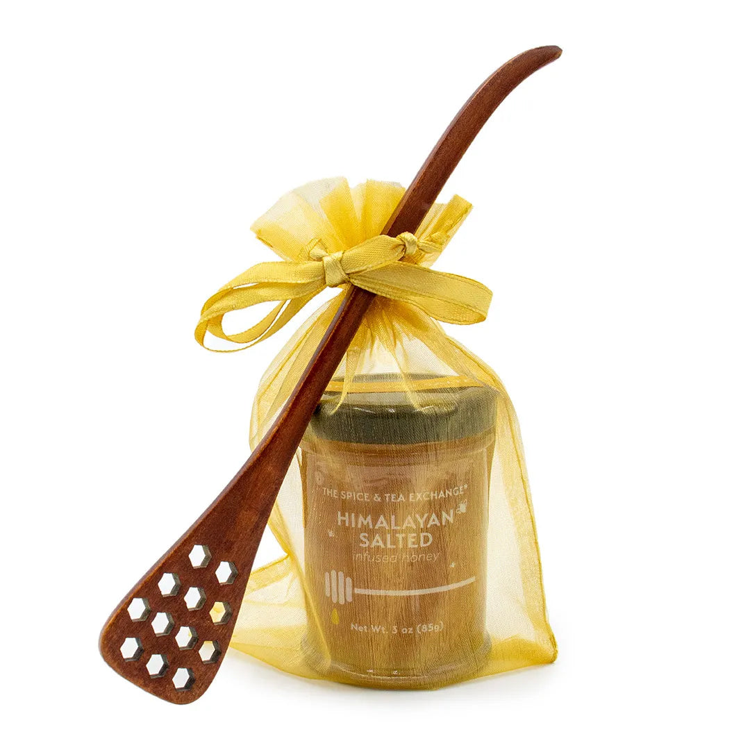 A Honey Jar with Dipper - Himalayan Salted is presented in a yellow organza gift bag tied with a ribbon, featuring a honeycomb wood dipper placed diagonally for a charming touch to this natural honey gift set.