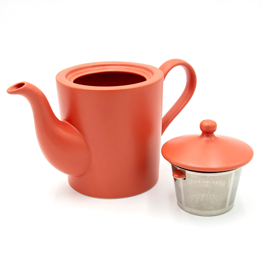 The Cactus Flower Teapot in matte orange with handle and spout is shown beside a tea mug infuser basket and matching orange lid, all set against a white background.